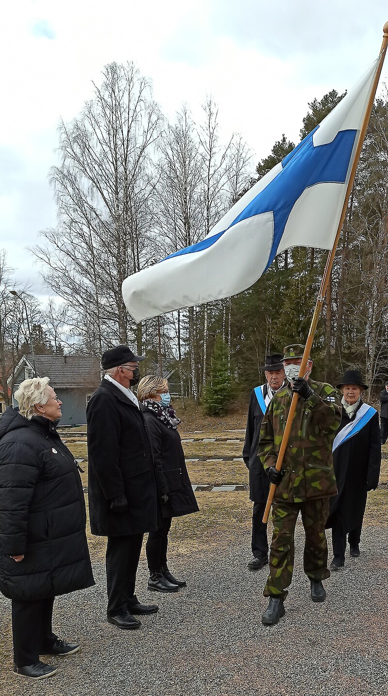 Suomen lippua seppeleenlaskussa kantoi Heikki Uusitalo ja airueina olivat Ulla ja Klaus Pentti. Seppelpartion jäsenet, kunnanvaltuuston pj Maarit Lepistö, kirkkovaltuuston pj Eero Norokorpi ja sotiemme veteraanien edustaja Arja Salonen seuraavat Suomen lipun poistumista. Kuva: Anu Mätäsniemi.