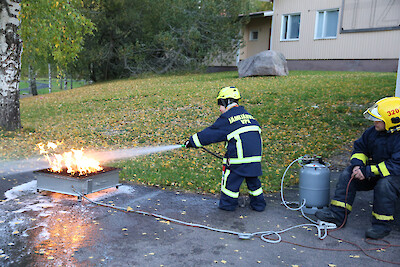 Henri Rantasalo sammuttaa paloa nestesammuttimella, ja harjoitusta valvoo Niko Koivumäki.