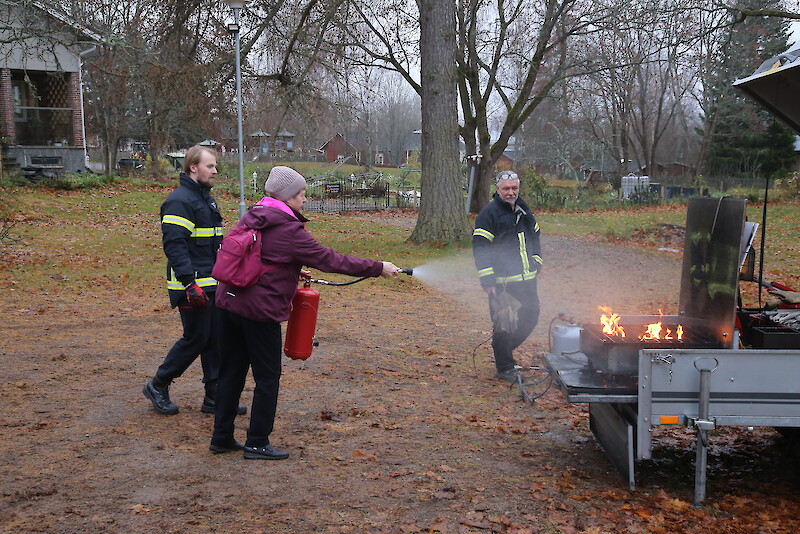 Kaija Salonen harjoittelee nestesammuttimen käyttöä, palomiehet Pauli Lukkarinen ja Markku Kukkula opastavat. Sammuttimen käyttöä Salonen on harjoitellut aikoinaan myös tehdastyössä järjestetyissä harjoituksissa.