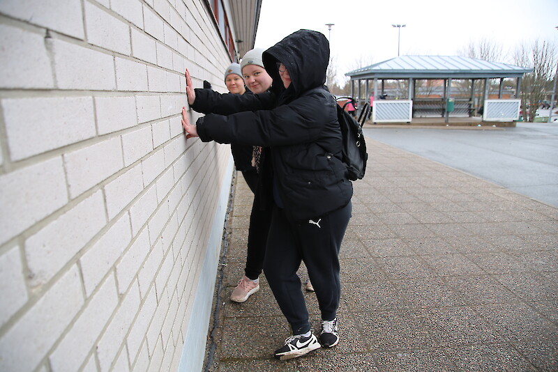 9-luokkalaiset Milla Vähävihu (vas), Anni Suoniemi ja Vilja Haapaniemi nojaavat vasten Jämijärven keskuskoulun toistaiseksi valkeaa seinää, joka saa väriä pintaansa myöhemmin keväällä.