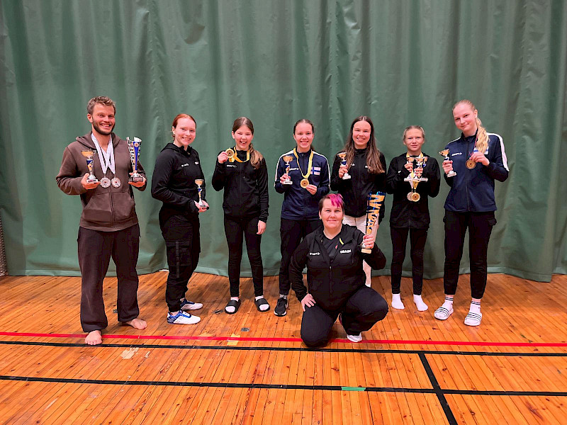 Mudo Sportsin menestyneitä ottelijoita yhteispotretissa Helsingissä. Kuvassa Terho Räsänen, Ella Järvenpää, Matilda Lappalainen, Enna Luiro, Emilia Koivunen, Adalmiina Vaittinen ja Helmi-Alina Rinneheimo. Edessä seurojen liigan pokaalin kanssa valmentaja Hanna Luiro.