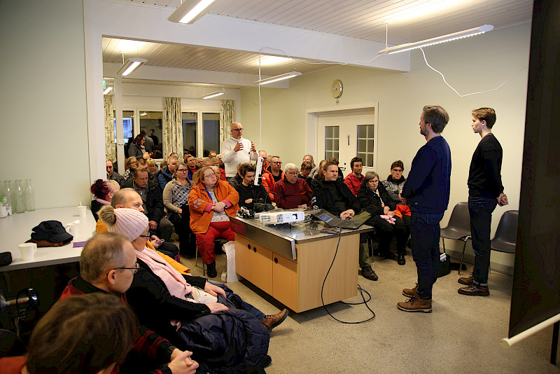 Kalliomäen tuulivoimahankkeen esittelytilaisuus houkutteli Toivolan lavalle noin 80 osallistujaa. ”Kesäkarhelainen” Rauno Hautamäki epäili tuulivoimaloiden kannattavuutta, kun niiden sähköntuotanto ja sähkön markkinahinta vaihtelevat hurjasti. Etualalla seisomassa hanketta valmistelevan Pohjan Voiman toimitusjohtaja Tomi Mäkipelto ja projektiassistentti Tuomas Westerling.