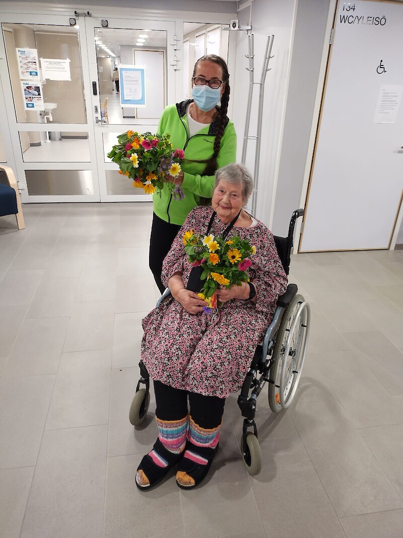 Katariina Pylsy ja 91-vuotias Irja Sarkki asettuivat yhteiskuvaan kukkakimppujen kanssa. – Oli ihana saada niin kauniita kukkia. Niin harvoin saan kukkia, se oli ihana piristys päivään, Sarkki kertoo. Kuva: Niclis Pylsy