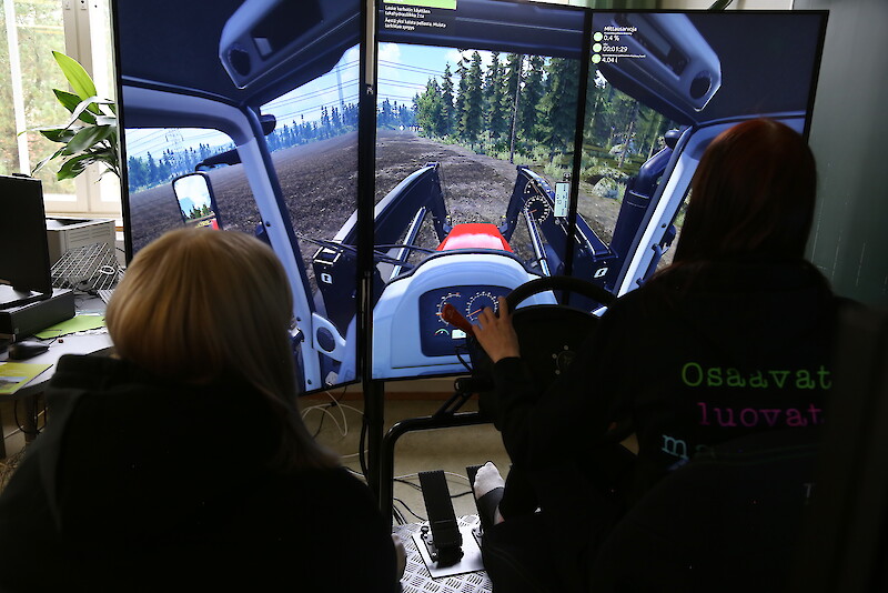 Janika Peltoniemi seuraa, kun Oona Tienari äestää traktorisimulaattorilla.